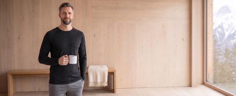 A+ Bild: Mann in Thermowäsche mit Tasse in einer Holzhütte